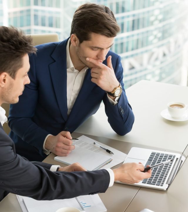 Business partners using laptop while working together on important corporate project in office. Businessman attentively listening to adviser Investment specialist making presentation of promising deal